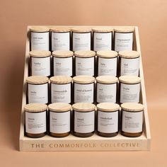 twelve jars of candles are arranged in a wooden display case on a beige background with the words, the commonsfok collective