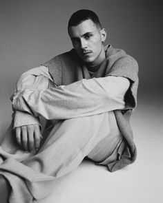 a black and white photo of a young man sitting on the floor wearing a sweater