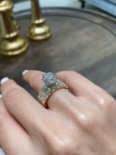 a woman's hand with a diamond ring on top of her finger, next to a golden candle holder