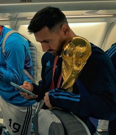 a man sitting on an airplane holding a soccer ball in his hand and looking at his cell phone