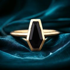 a gold ring with a black stone in the center on a blue velvet cloth background