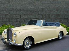 an old yellow car parked in front of a brick wall