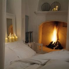 a bed with white sheets and candles in front of an open fire place on the wall