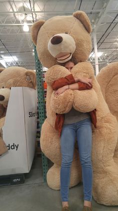 a woman is hugging a giant teddy bear in a store with other large teddy bears behind her