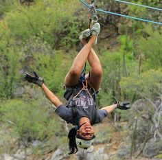 a man hanging from the side of a rope while riding on top of a zip line