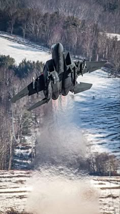 an air force jet is flying low over the snow covered ground in front of trees