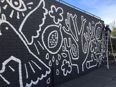 a man is painting the side of a black brick wall with white graffiti on it