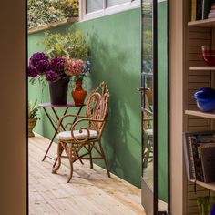 a chair and table on a wooden floor next to a green wall with potted plants