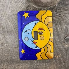 a painted sun and moon light switch cover on a wooden surface with wood planks