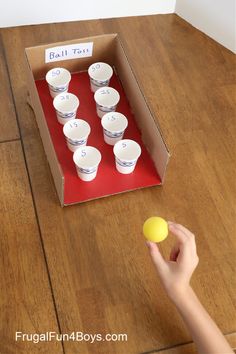 a child's hand holding an egg in front of a box with cups on it