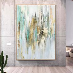 an abstract painting hangs on the wall above a cactus in a living room with wood flooring