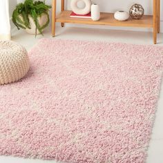 a pink rug in a living room next to a wooden shelf and potted plant