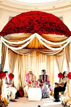 the bride and grooms are sitting in front of an elaborate canopy decorated with red flowers