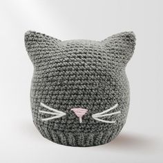 a crocheted gray cat hat with pink nose and ears is shown in front of a white background