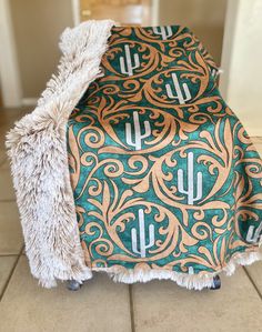 a green and gold patterned blanket with fringes on it sitting on a tile floor