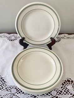 two white plates with green trim sit on a lace doily next to each other