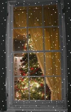 a christmas tree is seen through an open window with snow falling on the windowsill