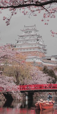 a small boat floating on top of a river next to a tall building with cherry blossom trees