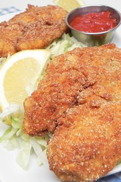 two fried fish fillets on a plate with lettuce and lemon wedges