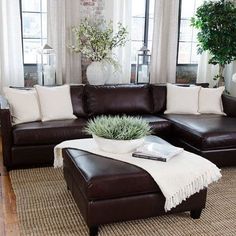 a living room with brown leather couches and white pillows on top of the rug