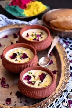 three small bowls filled with soup on top of a wooden tray next to bread and flowers