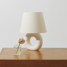 a white vase with a flower in it next to a lamp on a wooden table