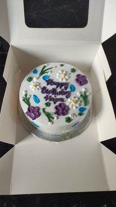 a birthday cake in a white box with purple and blue flowers on the side,