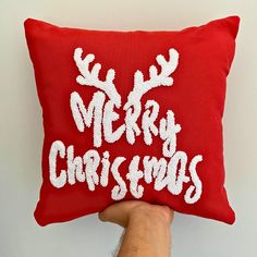 a hand holding a red christmas pillow with the words merry christmas written on it in white letters