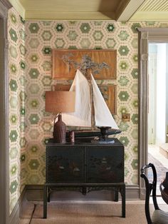 a sailboat is sitting on top of a dresser in a room with green and white wallpaper