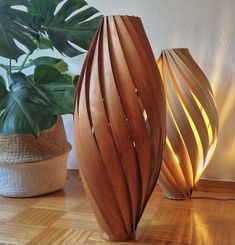 two wooden vases sitting on top of a hard wood floor next to a potted plant