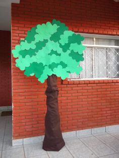 a tree made out of paper sitting in front of a brick building with a window