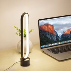 a laptop computer sitting on top of a wooden desk next to a lamp and vase