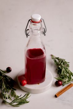 a bottle filled with liquid next to cinnamon sticks and cranberry sauce on a white surface