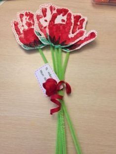 three red flowers with green stems on a table next to some pens and paper clips