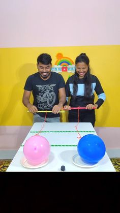 two people standing in front of a table with balloons on it