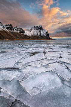 an icy landscape with mountains and clouds in the background at sunset or sunrise, as seen from across the frozen water