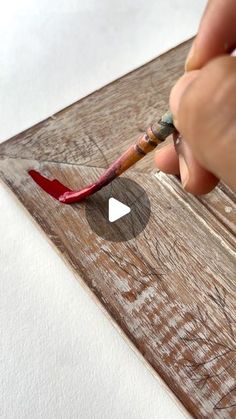 someone is using a paintbrush to draw something red on the wooden surface with their thumbnails