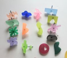 many different colored plastic objects are arranged on a white surface with pins in the shape of flowers