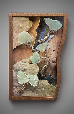 a piece of wood with sea glass in it's frame on the wall next to another piece of driftwood