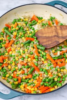 peas, carrots and peas are mixed together in a skillet with a wooden spoon