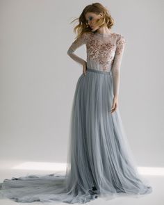 a woman in a long gray dress with sheer top and tulle skirt, standing against a