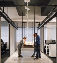 two people standing in an office looking at something on a table that is being held up