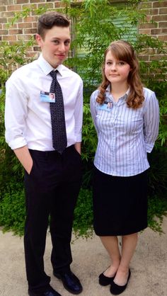 a man and woman standing next to each other in front of some bushes with green plants