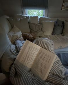 an open book laying on top of a bed next to pillows and a teddy bear