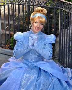 a woman in a blue dress sitting on a bench wearing a tiara and smiling at the camera