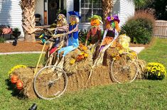 three scarecrows riding on top of hay bales in front of a house