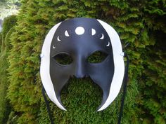 a black mask with white trim and eyes on top of a moss covered tree trunk