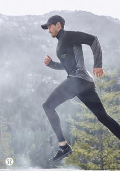 a man running in the rain wearing a black hat and grey shirt with trees behind him