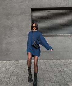 a woman in a blue sweater dress and black boots is holding her hand out to the side