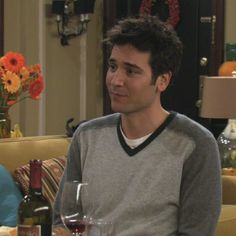 a man sitting on a couch next to a table with wine glasses and bottles in front of him